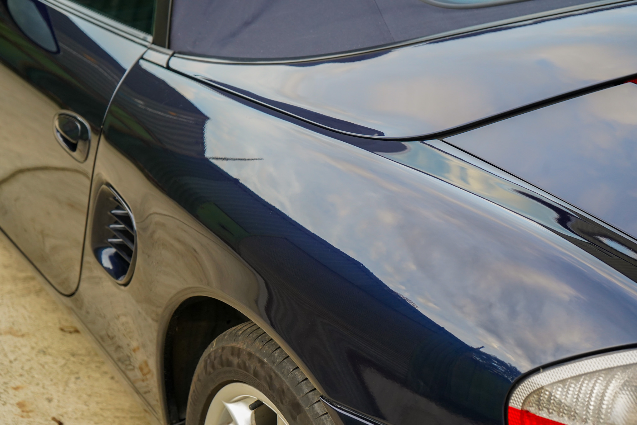 Dark blue 2003 Porsche Boxster (986) showing the rear quarter intake and soft top detail.