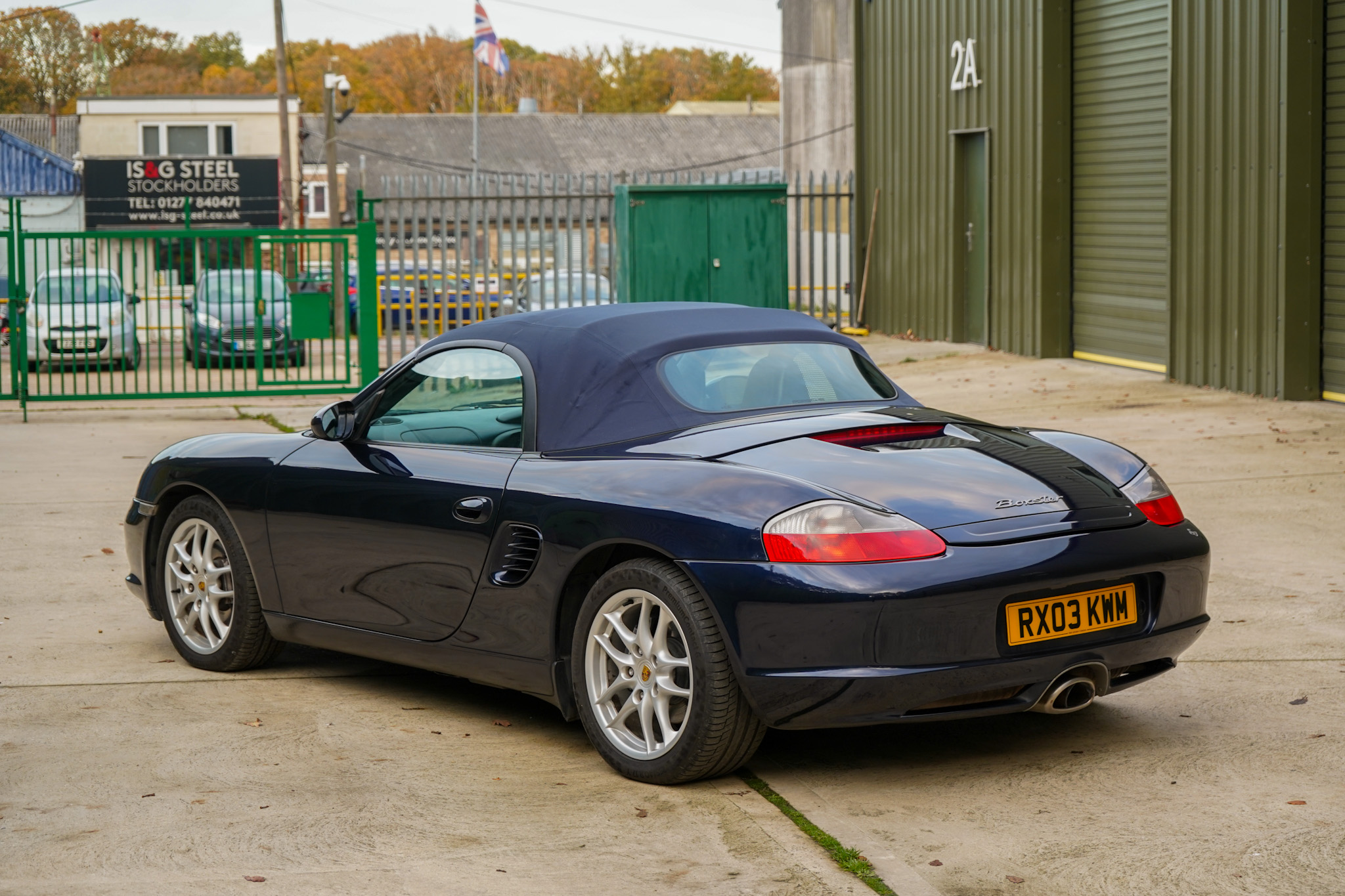 Dark blue 2003 Porsche Boxster (986) in a wide rear three-quarter view with the soft top raised.