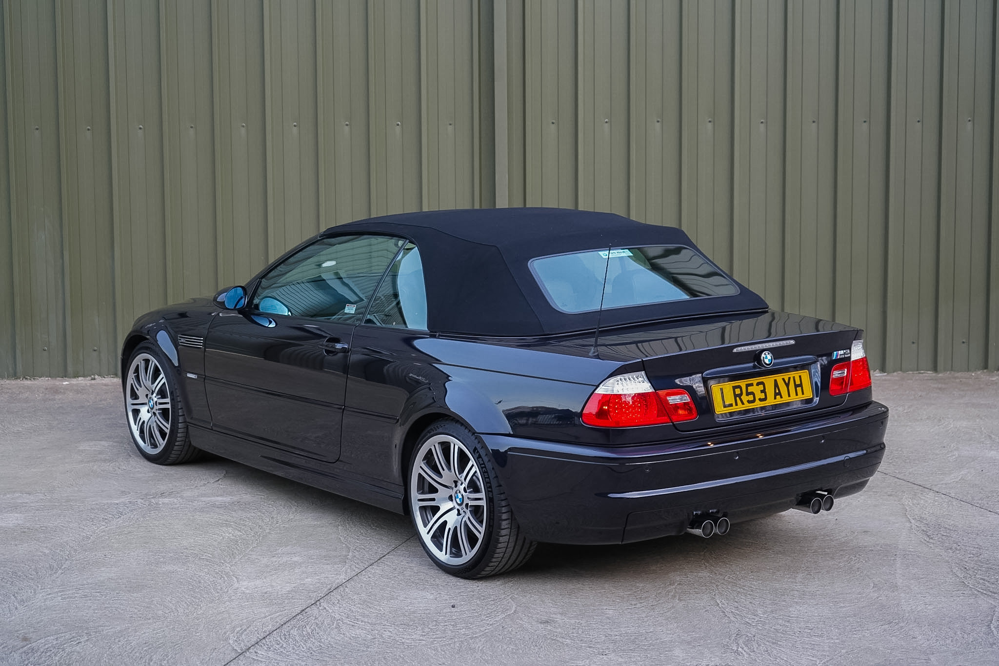 Carbon Black 2003 BMW M3 (E46) Convertible in a wide rear three-quarter view with the soft top raised.