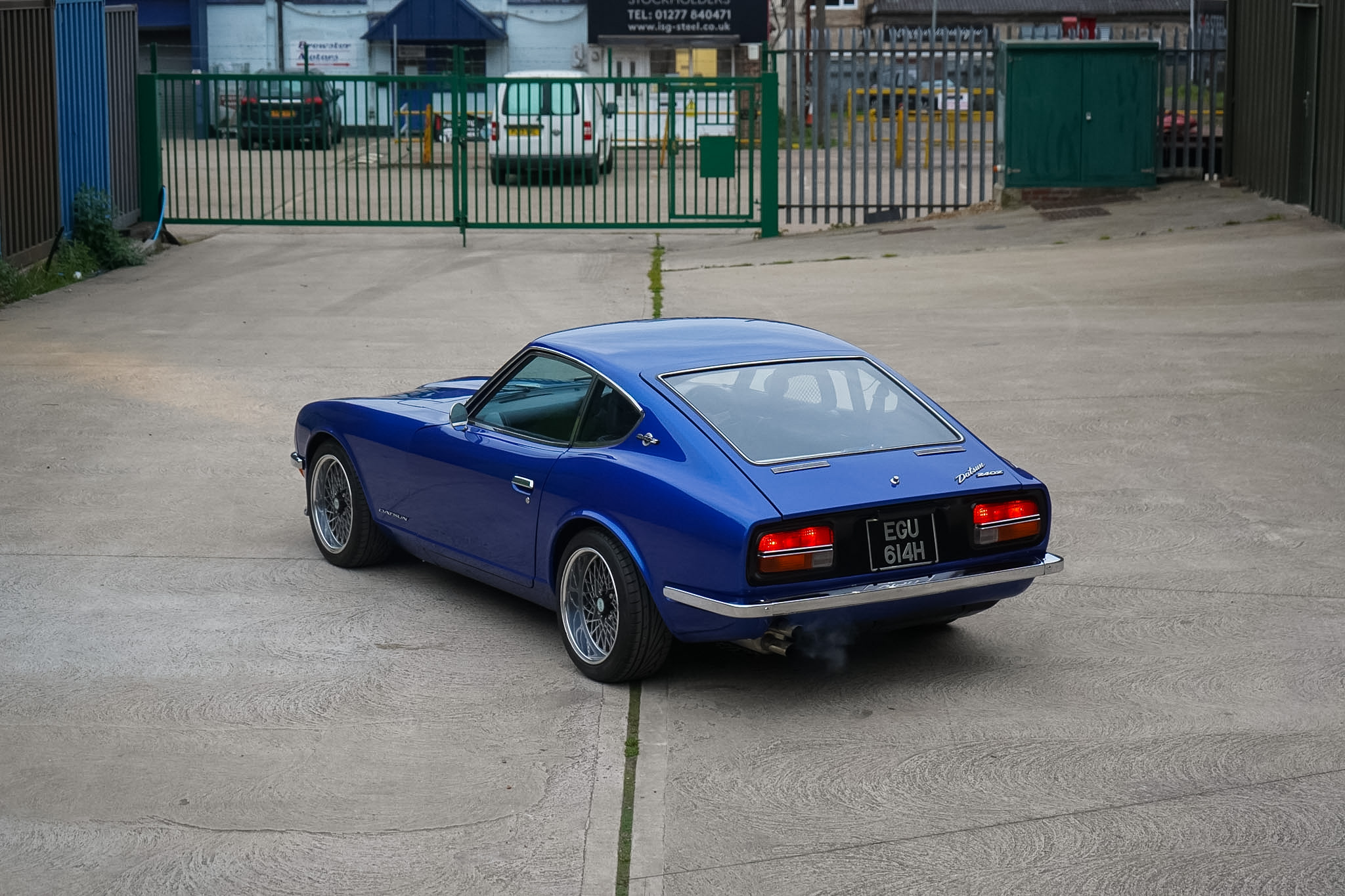 Blue Datsun 240Z Restomod wide rear three-quarter view in open yard.