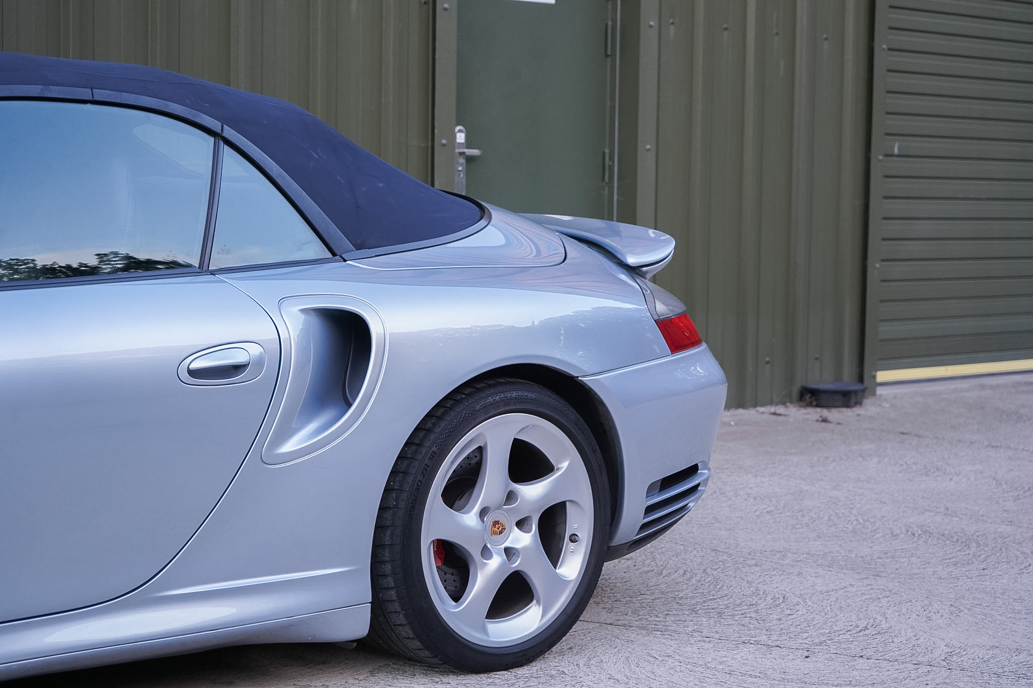 Silver Porsche 911 (996) Turbo X50 Cabriolet rear-quarter side-intake detail with soft top raised.